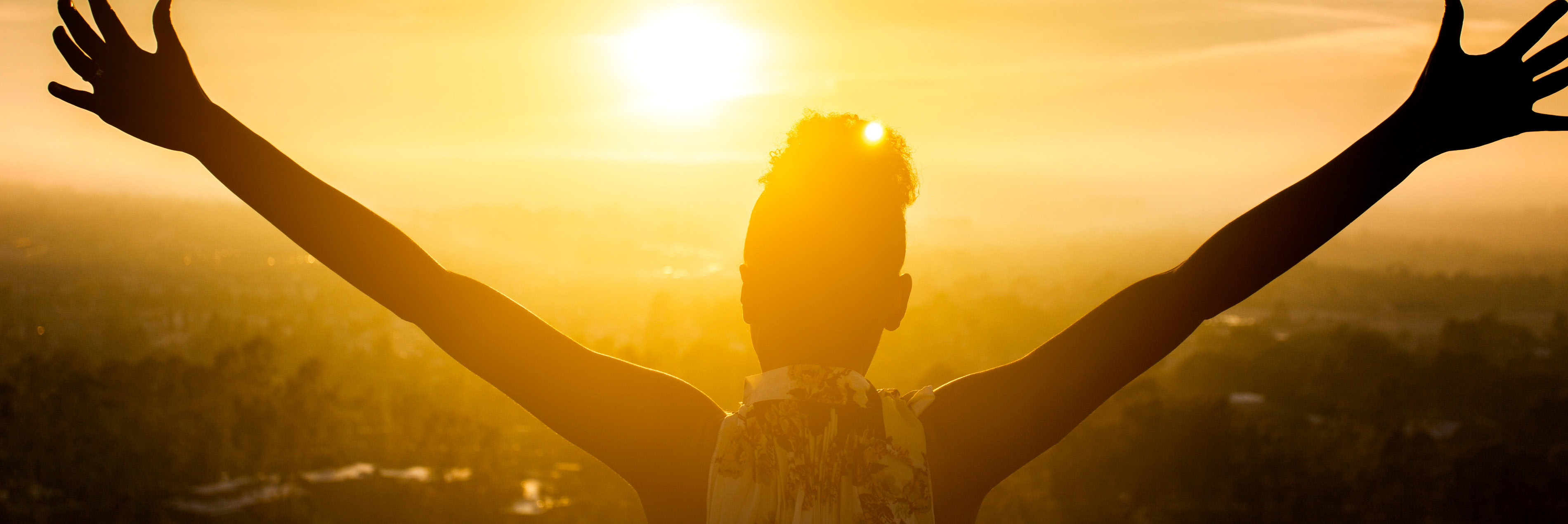 photo of woman with arms spread out looking at the sun